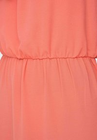 Gros plan sur un tissu rose corail avec une ceinture élastique froncée créant de doux plis.
