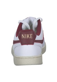 Sneaker Nike bianco con accenti rossi, caratterizzato da una tomaia in pelle texturizzata, colletto imbottito, linguetta posteriore esagonale e suola in gomma maculata.