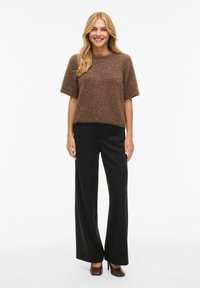 Brun strikket genser med korte ermer kombinert med svarte vide bukser og brune høyhælte sko. Glatt tekstur, ledig passform.