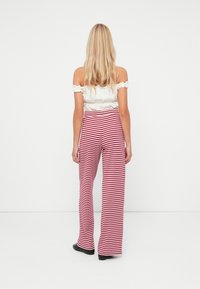 Calças largas listradas em vermelho e branco com cintura alta, combinadas com uma blusa branca sem alças, vistas de costas.
