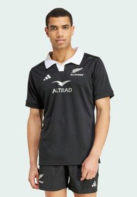 Sort rugbytrøje med hvid krave, der har All Blacks-logoet og Altrad-branding. Kortærmede, lavet af glat stof. Sorte shorts inkluderet.