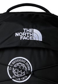 Black backpack featuring the white embroidered logo of The North Face and a circular patch with "THE GEODESIC DOME" text and geometric design.