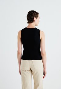 Zwarte mouwloze top met een aansluitend ontwerp, gemaakt van zacht materiaal. De rug heeft een ronde halslijn en minimale naden. Gecombineerd met beige broek.