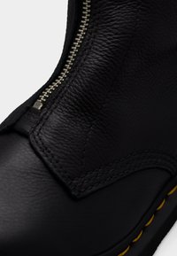 Μαύρο δερμάτινο μποτάκι αστραγάλου με πλαϊνό φερμουάρ, ραμμένες λεπτομέρειες και κίτρινο περίγραμμα. Η υφή είναι λεία με έναν ελαφρώς ματ φινίρισμα.