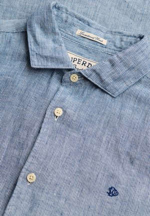 Lyseblå, stribet skjorte med knapper, hvide knapper, krave med foldede kanter og broderet lille blåt fiskelogo på brystet.
