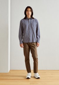 Blau-weiß kariertes Hemd, mit Knöpfen und langen Ärmeln, braune Hose und weiße Sneakers. Einfaches Design, glatte Textur.