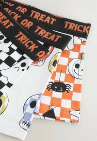 Trzy pary skarpet Halloweenowych z motywem "Cukierek albo Psikus" w czarno-pomarańczowych kolorach, z wzorami duchów, czaszek i pająków na kontrastowych tłach.