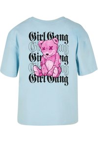 Gaiši zils T-krekls ar lielu rozā multfilmu lāča grafiku un melnu tekstu "Girl Gang", kas atkārtojas aiz lāča. Īsas piedurknes, brīva piegriezuma.