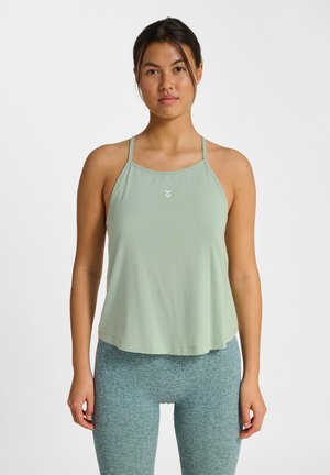 Kvinde iført lysegrøn ærmeløs sportstop og grå leggings, stående mod en ensfarvet hvid baggrund.