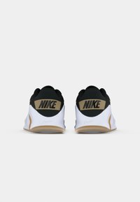 Sorte og gyldne Nike sneakers med en glat hvid sål. Bemærkelsesværdige funktioner inkluderer et stort sort "NIKE" logo på hælen og en afrundet form.