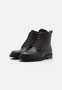 Bottines en cuir noir avec des accents texturés, bout rond et lacets. Présente un détail de logo sur le côté et une semelle en caoutchouc robuste.