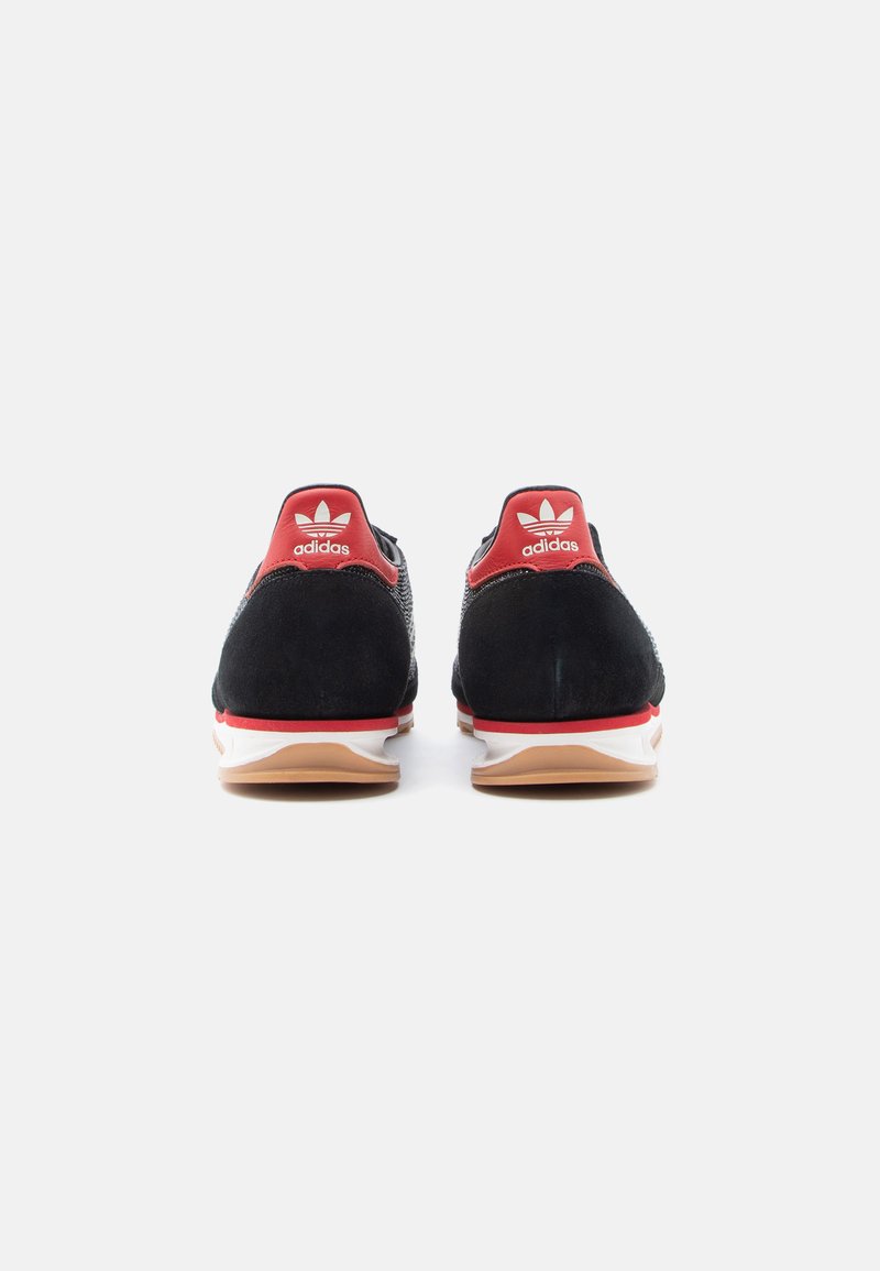 Black athletic shoes with red accents, suede and mesh upper, white midsole, and brown outsole. Adidas logo on heel and tongue.