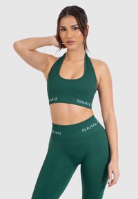 Sujetador deportivo verde oscuro y leggings a juego con una textura acanalada. El sujetador tiene un cuello halter y los leggings presentan una cinturilla con marca.