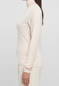 Helles rosafarbenes langärmeliges Rollkragenshirt aus weichem, glattem Stoff. Figurbetonter Schnitt mit schmalen Ärmeln und minimalistischem Stil, ohne Muster oder Akzente.