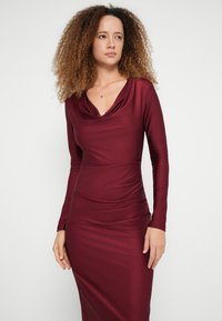 Bordové šaty s dlhým rukávom, siahajúce až po krk s volánmi a riaseným dizajnom po celej dĺžke, vyrobené z hladkej, elastickej látky. Priliehavý strih.