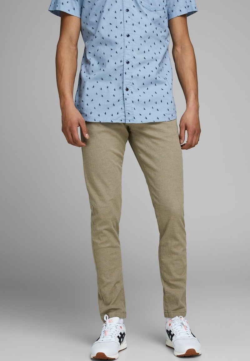 Short-sleeve light blue shirt with small black patterns, paired with beige slim-fit pants and white sneakers with black accents.