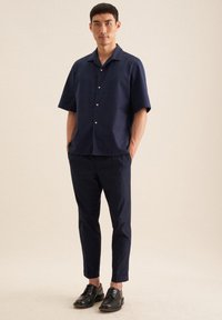 Middengroen overhemd met korte mouwen en een notch-kraag, gecombineerd met slim-fit middengroene broeken en zwarte veterschoenen.