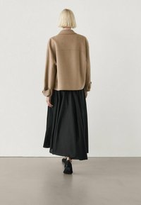 Beige oversized jacket with a black flowy skirt, both with smooth textures. The outfit is completed with black shoes.
