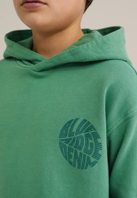 Sudadera de algodón verde con un gran diseño gráfico en azul marino en el pecho, con un corte relajado y capucha con cordón.