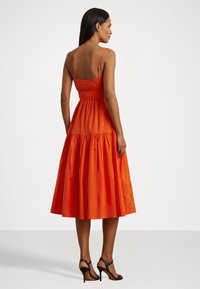 Vestido midi de algodão laranja com corpete justo, alças ajustáveis e saia ampla. Apresenta uma cintura franzida e uma textura suave.