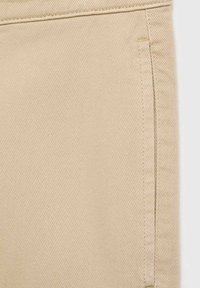 Gros plan sur un tissu beige montrant une texture détaillée de tissage diagonal et des coutures le long d'un bord de couture vertical.