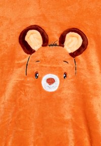Couverture en peluche orange avec un visage d'ours, des oreilles brunes, un museau blanc et des yeux noirs, le tout sur une texture douce et duveteuse.