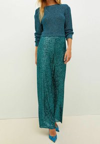 Woman wearing a teal knit sweater paired with high-waisted, teal sequin wide-leg pants and pointed blue heels.