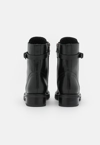 Schwarze Leder-Stiefeletten mit glatter Oberfläche, abgerundeter Spitze, zwei seitlichen Riemen und einem stabilen Absatz. Mit einem seitlichen Reißverschluss für ein einfaches An- und Ausziehen.