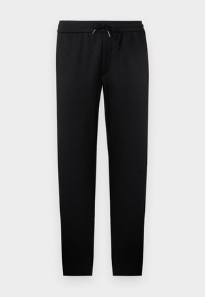 Musta tekstuuriinen vetoketjulliset jogger-housut, joissa on joustava vyötärönauha ja musta kiristysnyöri, kapenevat lahkeet ja resorit nilkoissa.