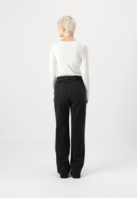 Jeans negri cu picioare largi, dotati cu două buzunare pe spate și talie înaltă, asortați cu un top alb ce prezintă ornamente asemănătoare perlelor pe mâneci.