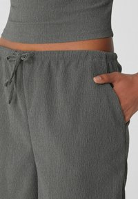 Pantaloni grigi con texture, dotati di vita elastica e coulisse, con tasche laterali e vestibilità rilassata. La finitura del tessuto è liscia.