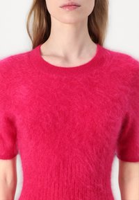 Flauschiger, kurzärmeliger Pullover in leuchtendem Pink. Verfügt über einen gerippten Ausschnitt und eine Textur mit einem gemütlichen, weichen Erscheinungsbild.