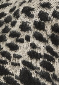Knit fabric featuring a beige background with black leopard spots, showcasing a soft texture and visible yarn pattern throughout.
