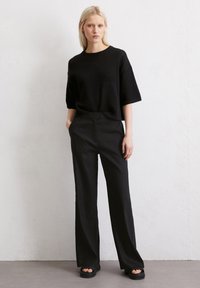 Zwart gebreid topje met korte mouwen, gecombineerd met zwarte broek met wijde pijpen. Textuurstof en een ontspannen pasvorm creëren een casual silhoeët.
