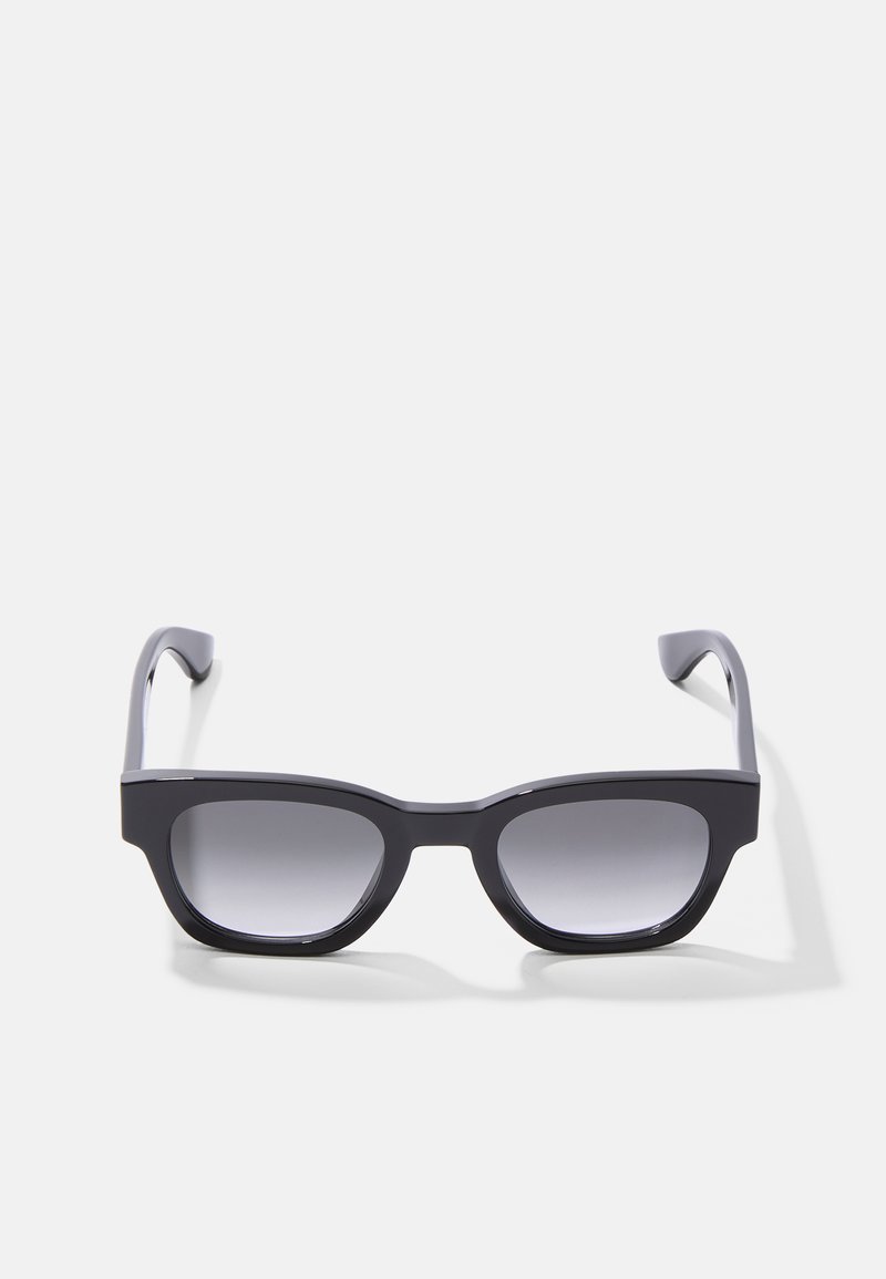 Schwarze Sonnenbrille mit rechteckigem Rahmen, ausgestattet mit dunklen, verlaufenden Gläsern und dicken Bügeln. Das Design weist glatte Flächen und minimale Akzente auf.