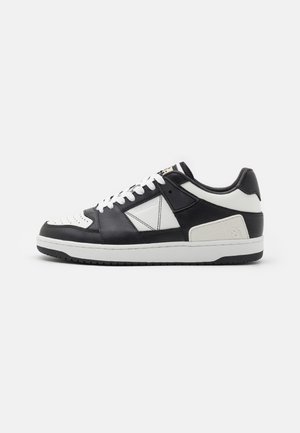 Sneaker in pelle bianca e nera con tomaia texturizzata, suola in gomma bianca, accenti a contrasto e dettagli perforati sulla punta.