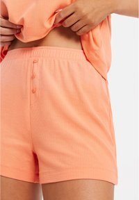Persikofärgade ribbade shorts med elastisk midja, fyra knappar och sidfickor, med en mjuk och slät textur.
