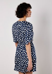 Kurzes, ärmelloses, navy-blaues Kleid mit einem weißen Herzmuster, geraffter Taille und geschwungenem Ausschnitt. Glattes Material, knielang, lockere Passform.