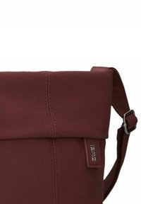 Bolso de cuero burdeos con tapa plegable, correa ajustable y herrajes de metal. Superficie texturizada y detalles de costura sutiles.