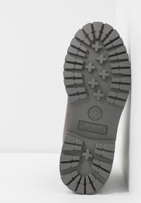 Semelle de botte Timberland marron avec un profond relief, présentant un motif unique d'hexagones et de croix, avec le logo embossé au talon.