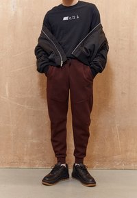 Černé dlouhé rukávy tričko s bílým logem Nike, spárované s burgundskými zúženými tepláky a černými teniskami s gumovými podrážkami.