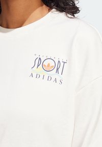 White cotton sweatshirt featuring a multicolored "SPORT" logo and three-stripe design accent. Relaxed fit with a crew neckline.