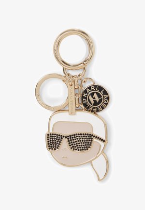 Llavero en tono dorado que presenta una cara estilizada con gafas de sol oscuras y una bufanda blanca. Incluye un charm de marca con un logo negro.