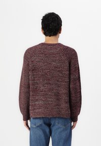 Strikkegenser i bordeaux og grå nyanser, med ribbestruktur, rund hals og avslappet passform. Kombinert med blå jeans.