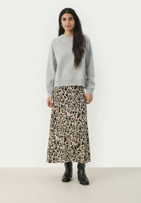 Grauer Pullover mit Rundhalsausschnitt, kombiniert mit einem langen Rock im Leopardenmuster. Schwarze Knöchelstiefel runden das Outfit ab.