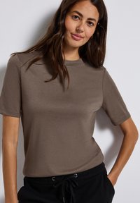 Brun kortärmad t-shirt i mjukt tyg med rund hals och avslappnad passform, stylad med svarta byxor med dragsko.