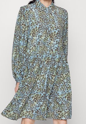 Mujer con un vestido suelto, de manga larga y con botones, con estampado de leopardo en verde y azul.