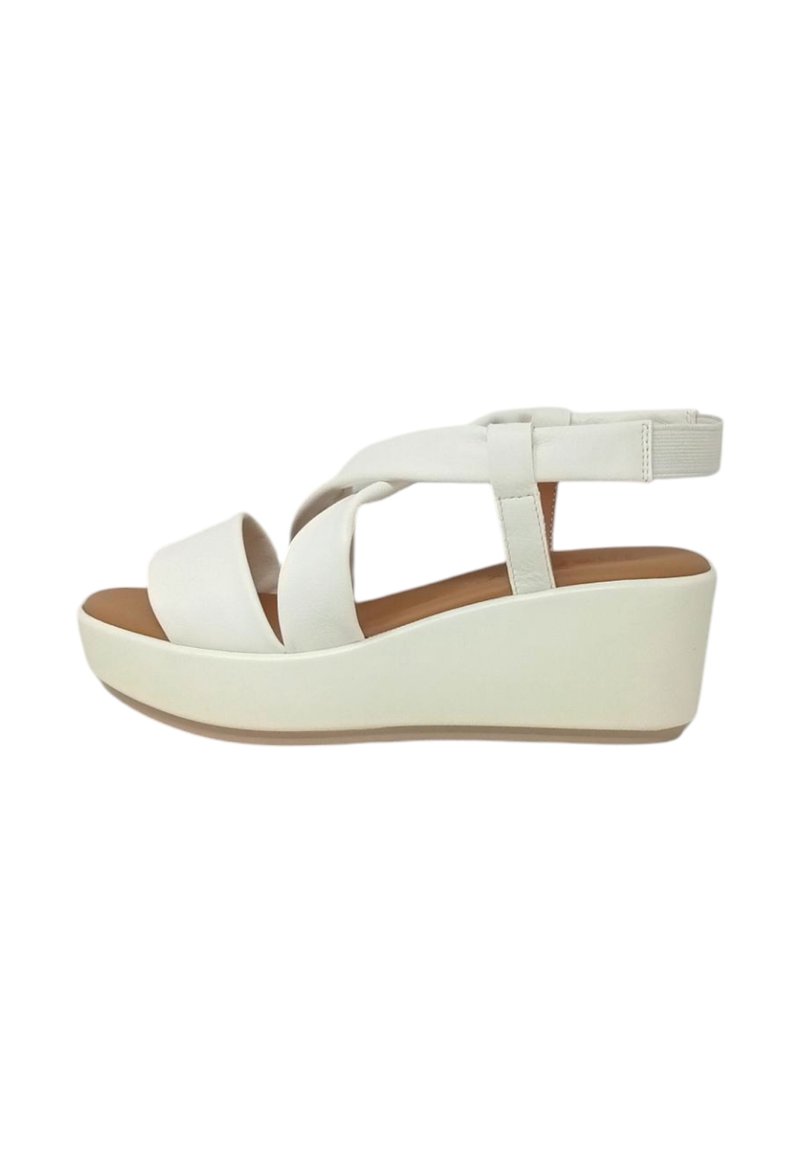 Sandali wedge bianchi con cinturini incrociati, una soletta imbottita e una finitura liscia e lucida. L'altezza del wedge scende gradualmente per offrire supporto.