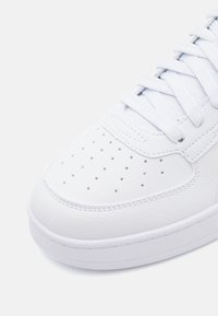 Adidași albi din piele, cu un upper neted și texturat, având perforații pe zona de la degete și șireturi groase, plate, de culoare albă.