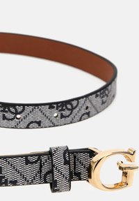 Ceinture en tissu à motifs noir et blanc avec une boucle en or en forme de lettre G, dotée d'un intérieur en cuir marron lisse et de cinq trous ajustables.